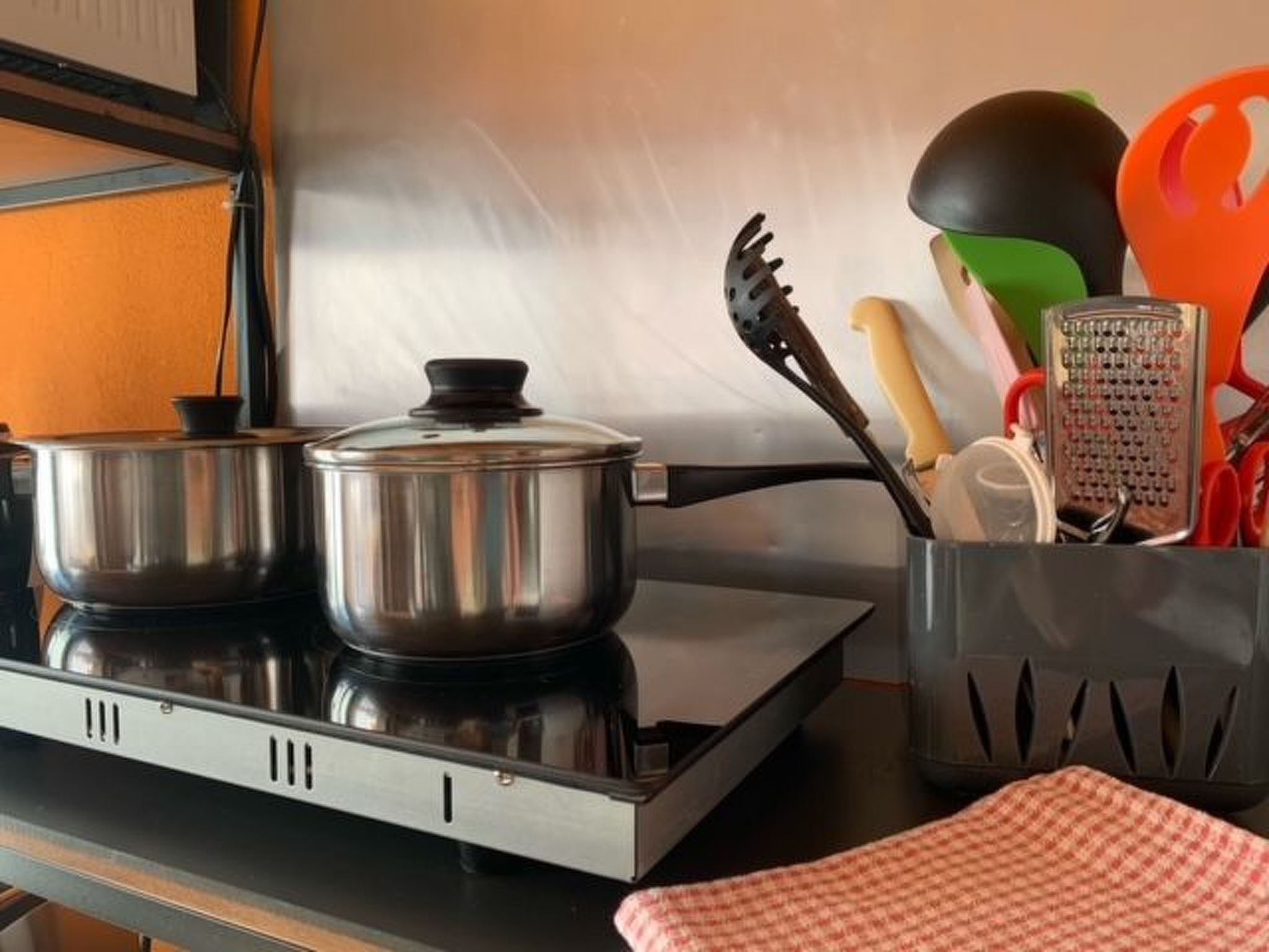 Cozinha com duas panelas de aço inoxidável em um fogão, um escorredor, um ralador e um utensílio de cozinha com cabo vermelho.
