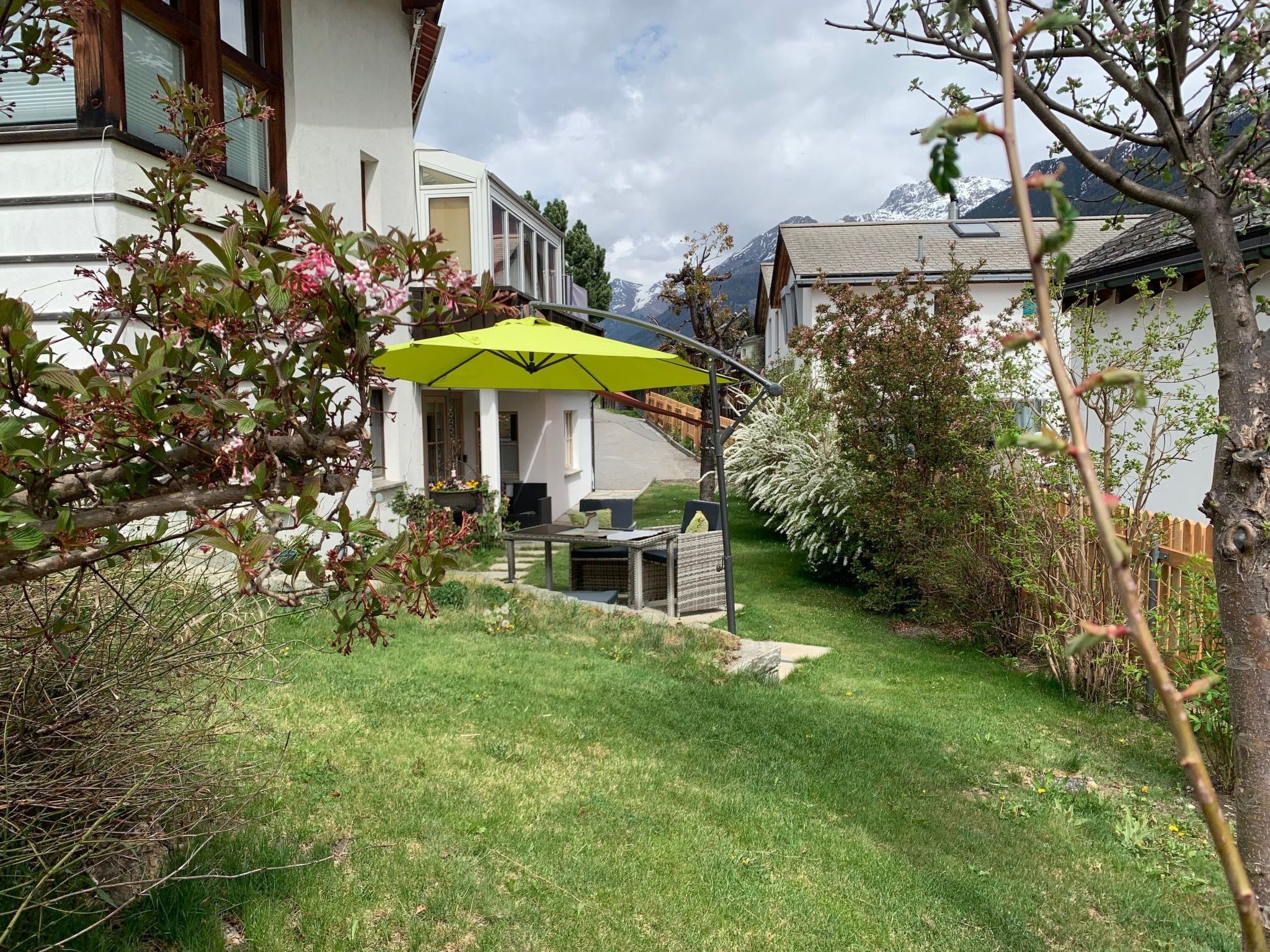 A residential garden with a patio area, a table, and a yellow umbrella.