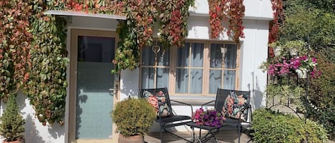 Ein Haus mit überdachter Veranda, zwei Stühlen und Kübelpflanzen.