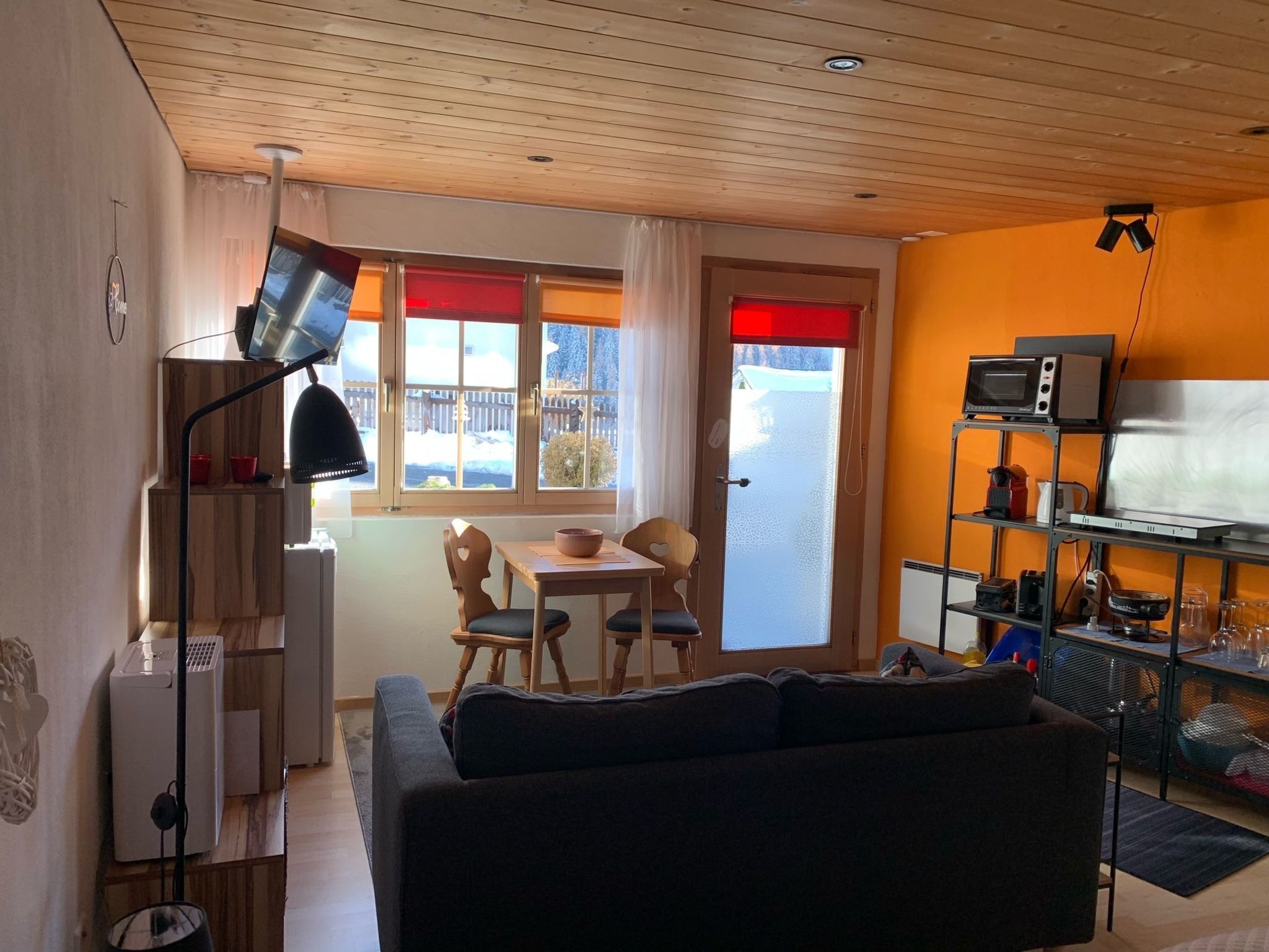 Un área de estar acogedora con un sofá, una mesa de comedor con sillas, una cocina con microondas y una ventana con vistas a un paisaje nevado.