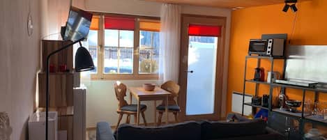 Un área de estar acogedora con un sofá, una mesa de comedor con sillas, una cocina con microondas y una ventana con vistas a un paisaje nevado.