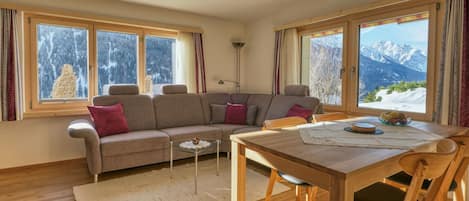 Un salon chaleureux avec un canapé, une table à manger et de grandes fenêtres offrant une vue sur les montagnes.