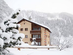 A two-story building with a balcony, surrounded by snow-covered trees and mountains. - Chasa Müfaits Parterre, (Tschierv) by Interhome (Tschierv)