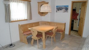 A dining area with a wooden table and benches, a pendant light, a window with curtains, and a kitchen visible through an open door. - Chasa Müfaits Parterre, (Tschierv) by Interhome (Tschierv)