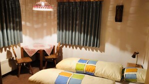 A cozy room with a bed, two pillows, a table with chairs, a hanging light fixture, and a window with curtains.