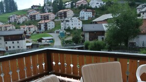 A balcony with two chairs and a table, overlooking a hillside village with houses.