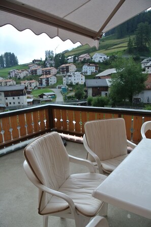 Un balcon avec deux chaises et une table, donnant sur un village perché sur une colline, avec ses maisons.