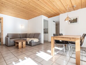 Un interior moderno con techo de madera, un sofá gris, una mesa de comedor de madera y una cocina al fondo.