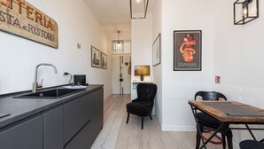 A modern kitchen with a black countertop, a sink, and a chair. There is a wooden table with chairs and a poster on the wall. - Golden Roof 4 by MMega (Florence)