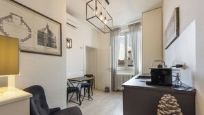 A modern hotel room with a dining area, a black chair, a table, a lamp, a radiator, and a framed architectural drawing on the wall. - Golden Roof 4 by MMega (Florence)