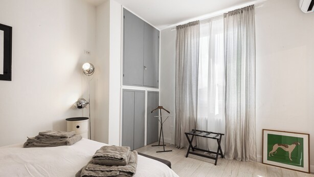 A hotel room with a bed, a bedside table, a hanging coat rack, a framed picture, and a window with curtains. - Golden Roof 4 by MMega (Florence)