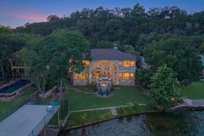 A stone house with a fire pit and outdoor seating, surrounded by a lush garden and a body of water. - 4BR Lake Austin Estate | Private Dock + Wake Surf Water | 200 Ft Frontage (Austin)