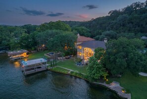 A lakeside property with a house, dock, and surrounding greenery. - 4BR Lake Austin Estate | Private Dock + Wake Surf Water | 200 Ft Frontage (Austin)