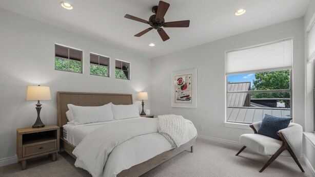 Ein Schlafzimmer mit einem Bett, Nachttischen, einem Deckenventilator, einem Fenster mit Blick und einem Sessel.