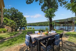 An outdoor dining area with a view of a lake, surrounded by trees and a deck. - 4BR Lake Austin Estate | Private Dock + Wake Surf Water | 200 Ft Frontage (Austin)