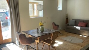 A dining area with a wooden table, chairs, and a vase of flowers. There is a sofa and a window in the background. - Stüvetta à Porta, (Scuol) by Interhome (Scuol)
