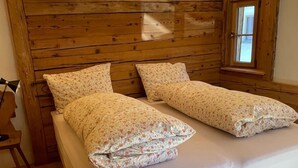 A room with a wooden ceiling, a bed with floral bedding, a wooden chair, and a window. - Stüvetta à Porta, (Scuol) by Interhome (Scuol)