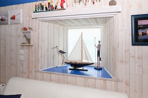 Una habitación con pared de madera, un velero modelo, una figura y una estantería con varios objetos.