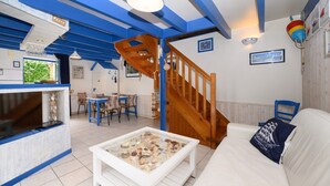 Una sala de estar con una escalera de madera, un sofá blanco, una mesa de centro de vidrio con conchas marinas y un televisor en una pared azul y blanca.