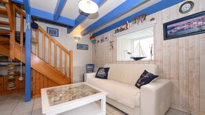 Una sala de estar con un sofá blanco, una mesa de centro de vidrio, una escalera de madera y un ventanal con vista a un velero.