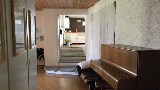 Een gang met een piano, een trap die naar een keuken leidt en een deur aan de linkerkant.