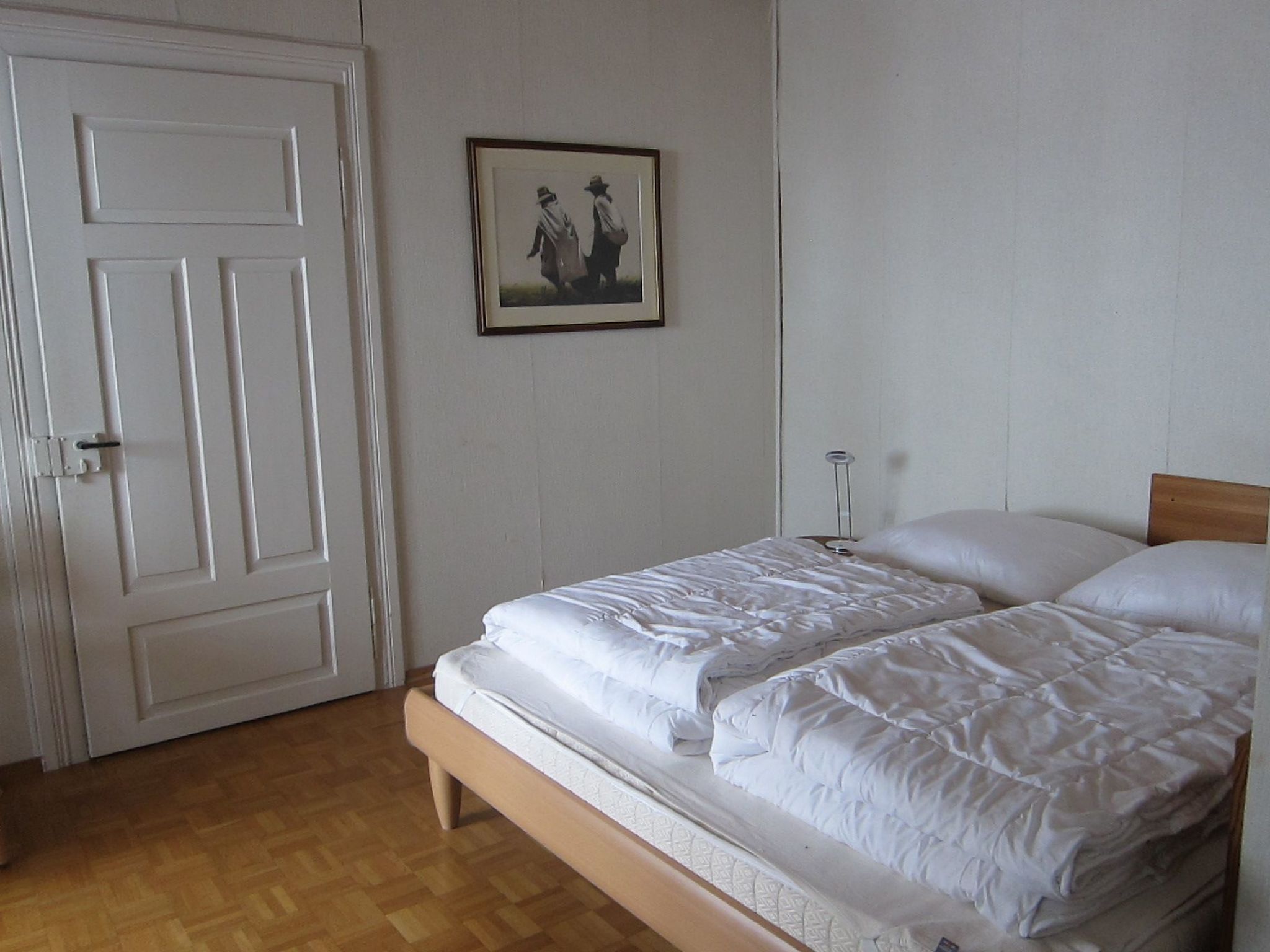 Un dormitorio con una cama doble, una puerta y un cuadro en la pared.