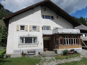 Ein zweistöckiges Gebäude mit Balkon, Veranda und einem gepflasterten Weg zum Eingang.