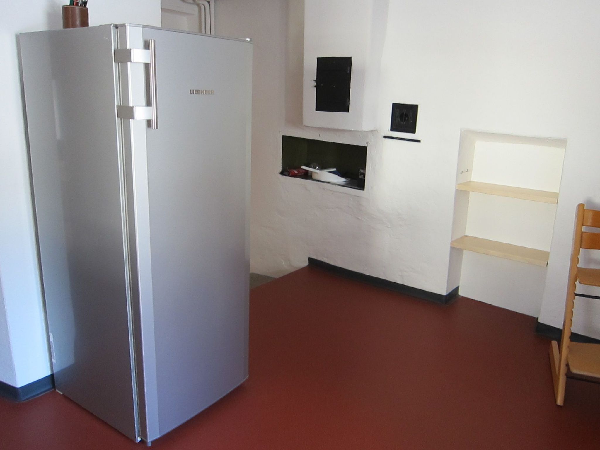Une cuisine avec un réfrigérateur en acier inoxydable, une chaise en bois et un meuble blanc.