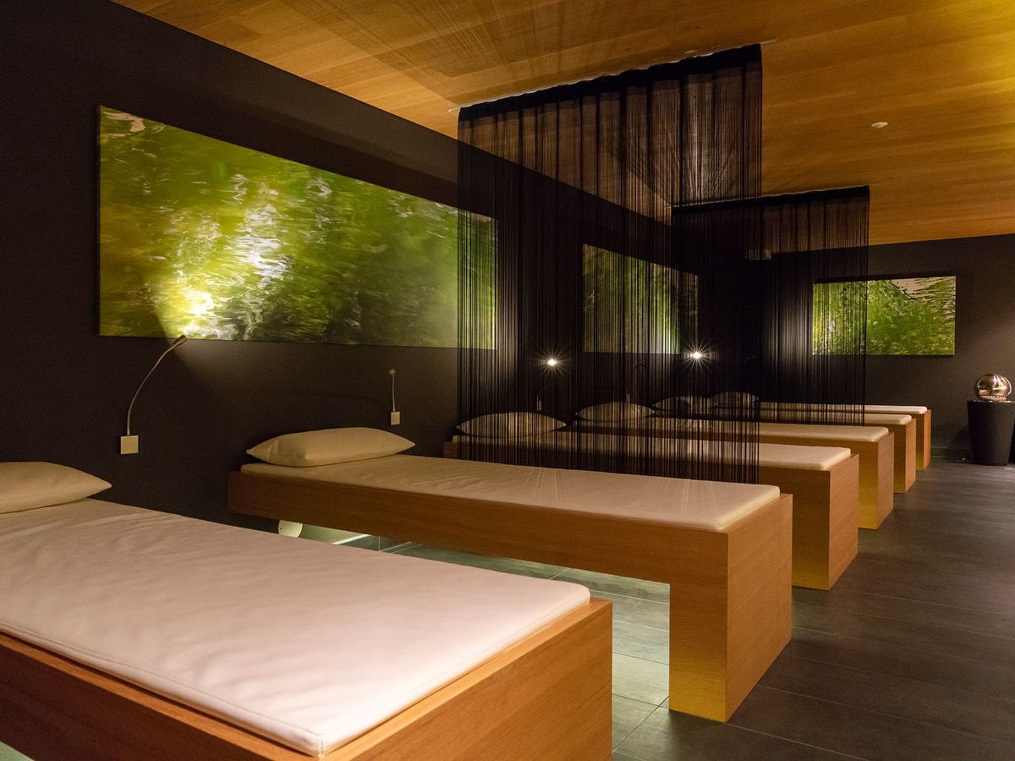 Un spa moderno con bancos de madera, un cuadro abstracto grande de color verde y una partición oscura.