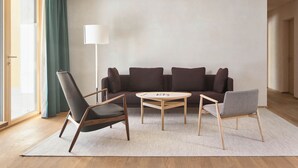 Una sala de estar moderna con un sofá, dos sillones, una mesa de centro, una lámpara de pie y un ventanal con cortinas.