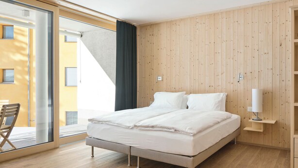 Un dormitorio moderno con una cama grande, paneles de madera en las paredes, un ventanal y una silla junto a la ventana.