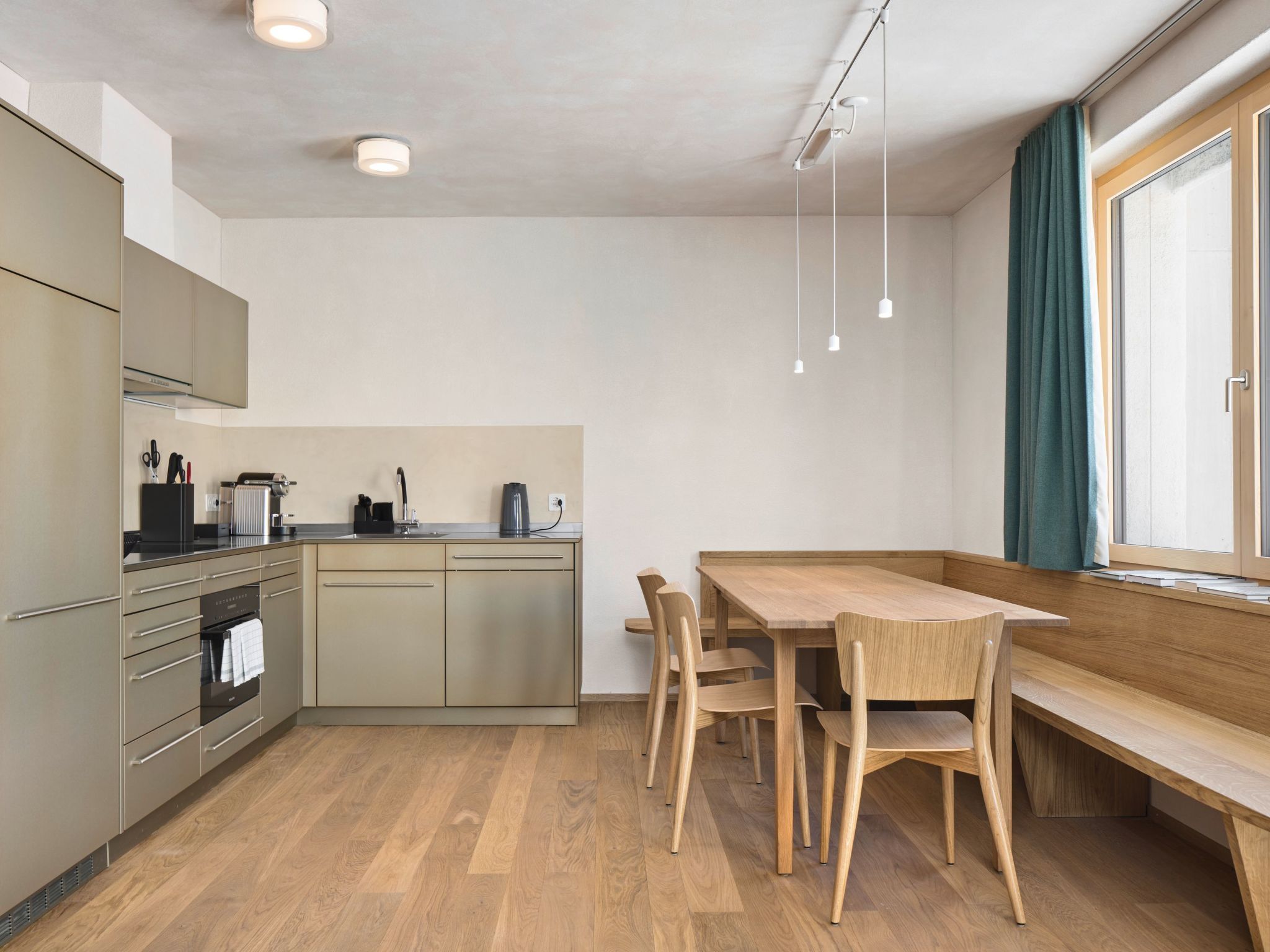 Una cocina moderna con una mesa y sillas de madera, un horno empotrado y una ventana con cortinas.