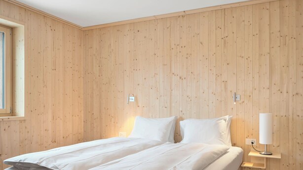 A bedroom with a wooden paneled wall, a bed with white bedding, bedside lamps, and a window. - Hotel Maistra 160, (Pontresina), by Interhome (Pontresina)
