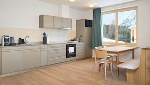 A modern kitchen with a dining area, wooden cabinets, a built-in oven, and a large window with a view of mountains. - Hotel Maistra 160, (Pontresina), by Interhome (Pontresina)