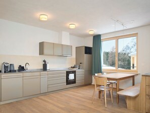 A modern kitchen with a dining area, wooden cabinets, a built-in oven, and a large window with a view of mountains. - Hotel Maistra 160, (Pontresina), by Interhome (Pontresina)