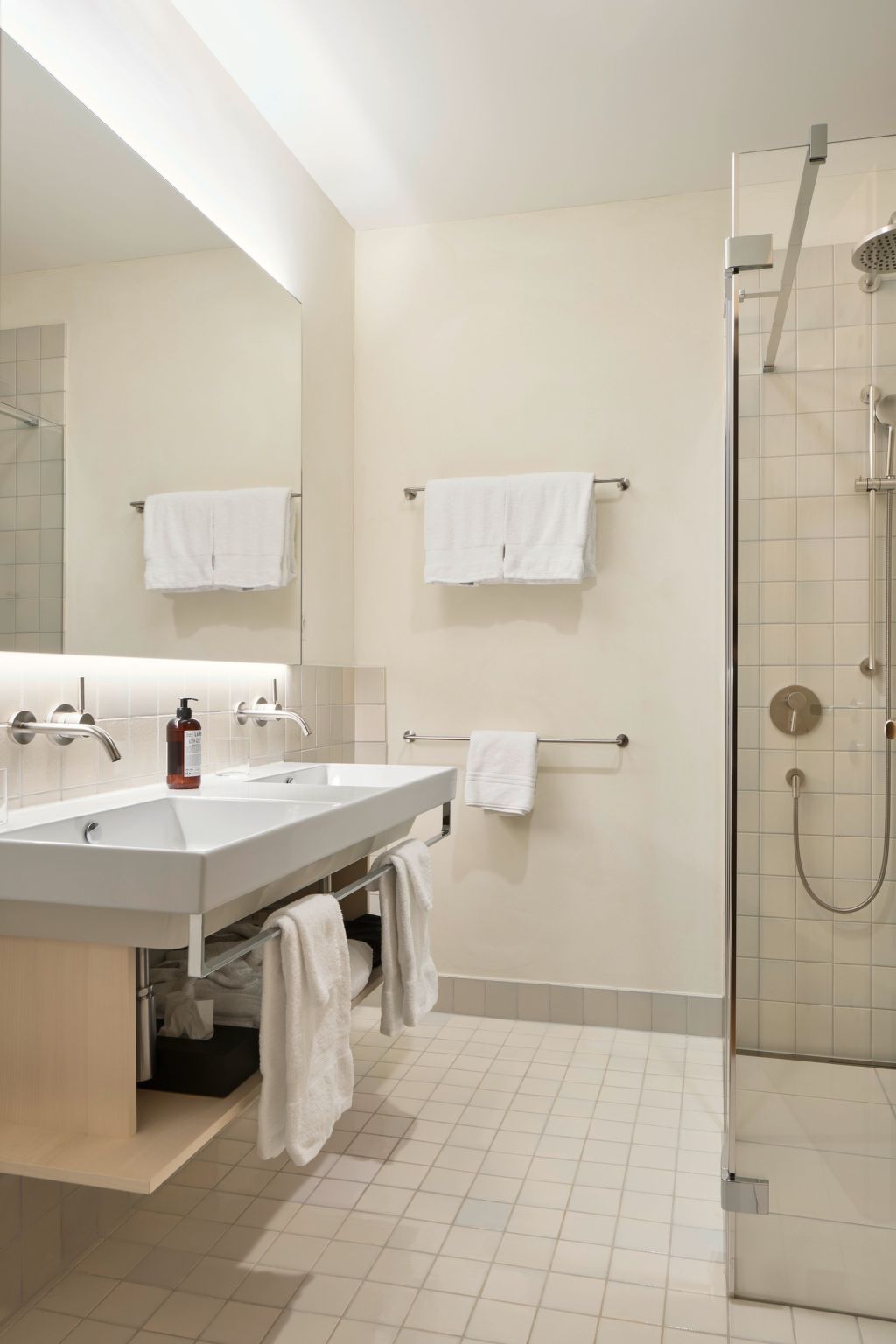 Un baño moderno con lavamanos doble, cabina de ducha con vidrio y dos toalleros.