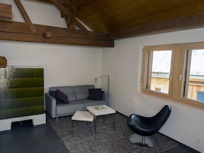 A modern living room with a grey sofa, a black chair, a small white table, and a window with wooden frames. - Chasa Tablà, (Guarda) by Interhome (Guarda)