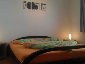 Una cama con un edredón y almohadas coloridos, una lámpara de noche y una pared con arte abstracto.