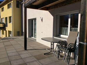 An outdoor patio area with a table and chairs, a window, and a door. - Fionas / Wohnung Vonlanthen, (Ftan) by Interhome (Ftan)