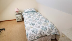 Un dormitorio pequeño y ordenado con una cama individual, una mesita de noche, una lámpara y un aparador.