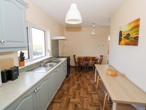 A kitchen with a wooden herringbone floor, a dining table with chairs, a hanging light fixture, and a window with a view. - Ocean View (Westport)