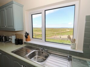 A kitchen with a stainless steel sink, a window with a view of a grassy field, and a utensil holder on the windowsill. - Ocean View (Westport)