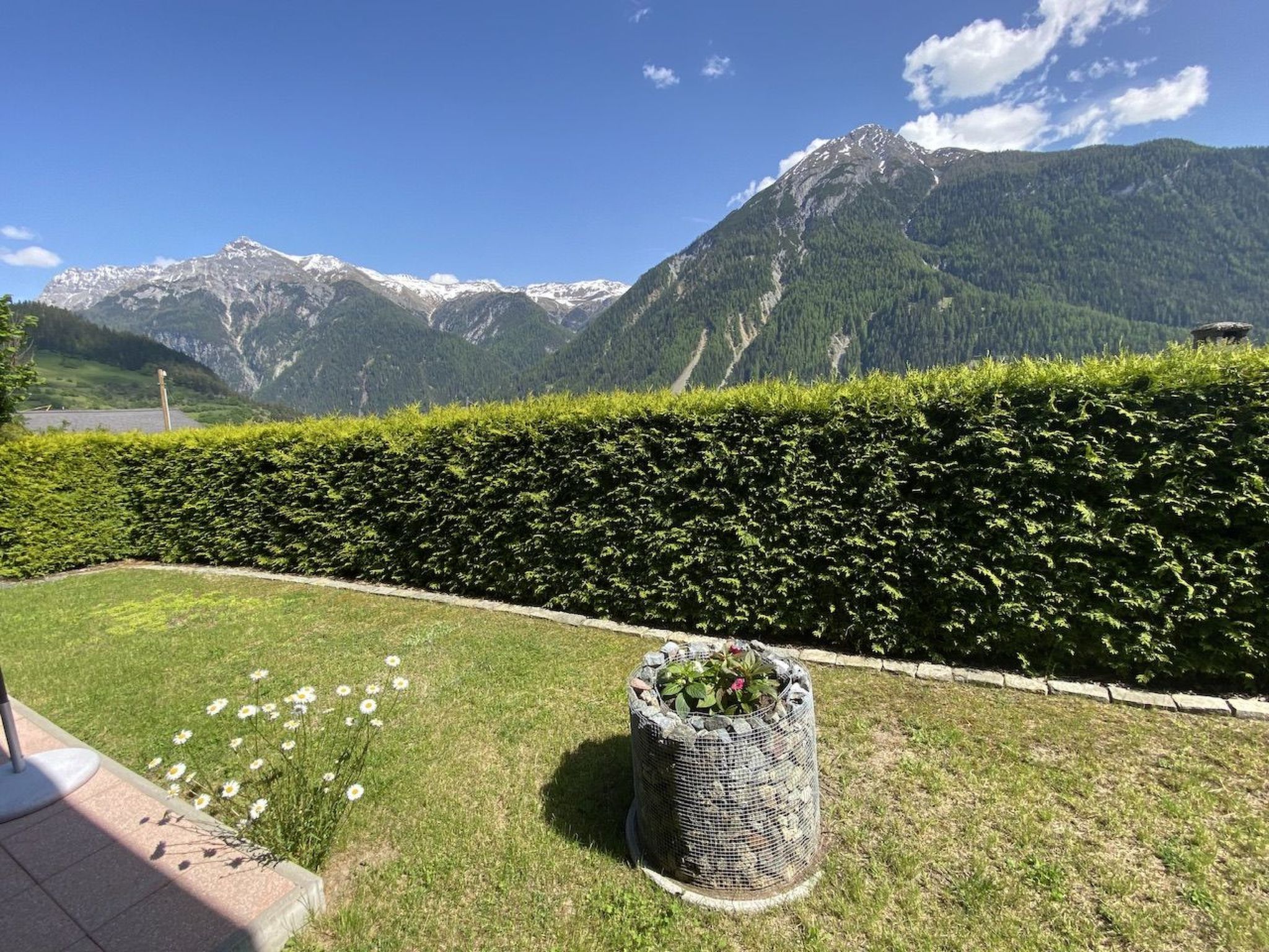 Jardim ajardinado com sebes, canteiros de flores e vista para montanhas nevadas.
