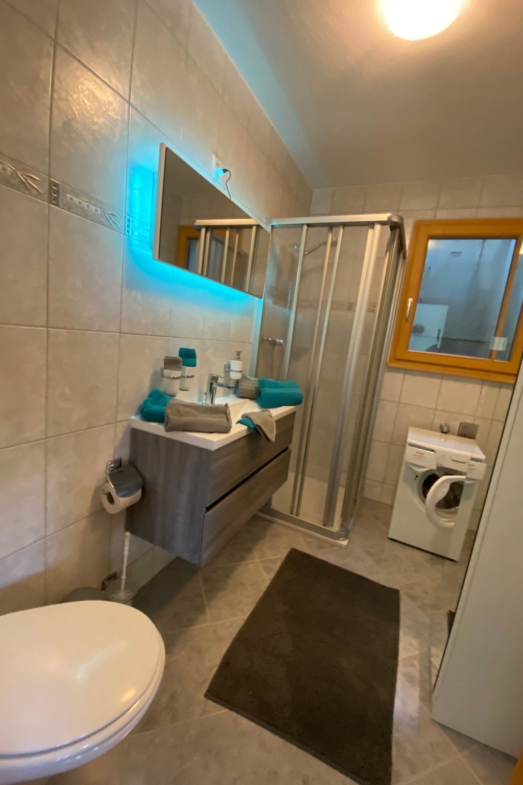 Ein Badezimmer mit Toilette, Waschbecken mit Spiegel, Dusche und Waschmaschine.