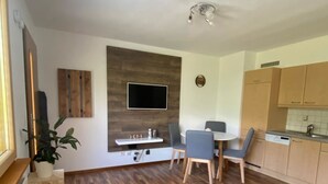 A modern living room with a wooden floor, a blue sofa, a dining area with a table and chairs, a kitchen with wooden cabinets, and a mounted TV. - Leitner, (Ramosch) by Interhome (Ramosch)