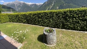 A garden with a stone planter and a hedge, a clear sky, and a mountain range in the background. - Leitner, (Ramosch) by Interhome (Ramosch)