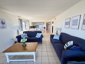 A living room with two sofas, a coffee table, and a kitchen in the background. - Oceanfront 3BR Condo w/ Sunrise Balcony, Pool, Parking & Convention Center Walk (Ocean City)