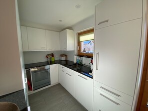 Eine kompakte Küche mit weißen Schränken, einem eingebauten Backofen und einem Fenster mit Blick ins Freie.