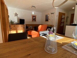En matplats med ett träbord, stolar, en vas med blommor och en tv i bakgrunden.
