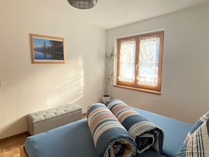 Een kamer met een bed, een bankje, een potplant en een raam met gezandstraalde glass.